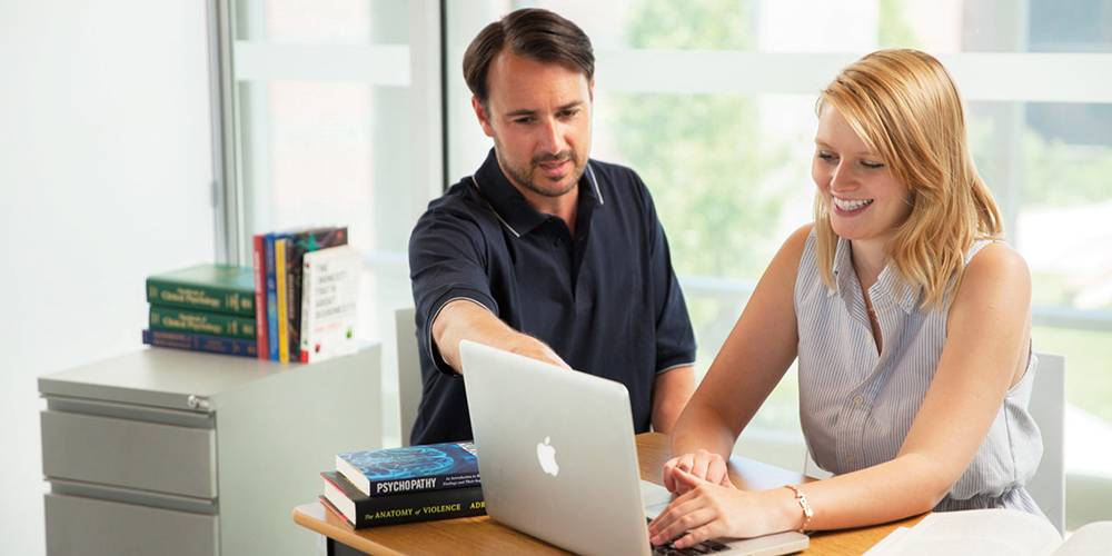 Two individuals working around a laptop with psychology textbooks around them.